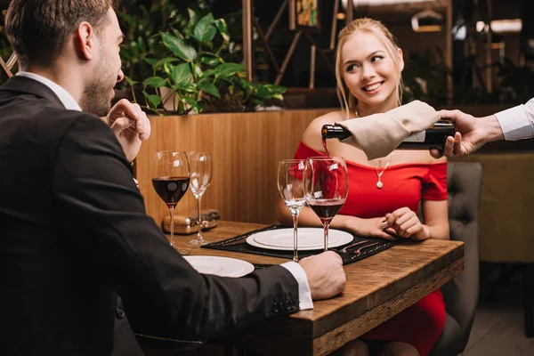 Cheerful girl looking at boyfriend while waiter pouring red wine into glass in restaurant — Stock Photo