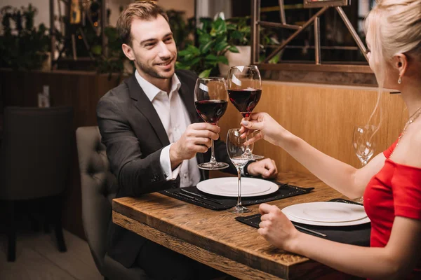 Hombre alegre tostadas con vino tinto y sonriendo a la novia en el restaurante - foto de stock