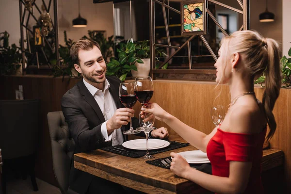 Cheerful man toasting with wine and smiling to girlfriend in red dress — Stock Photo