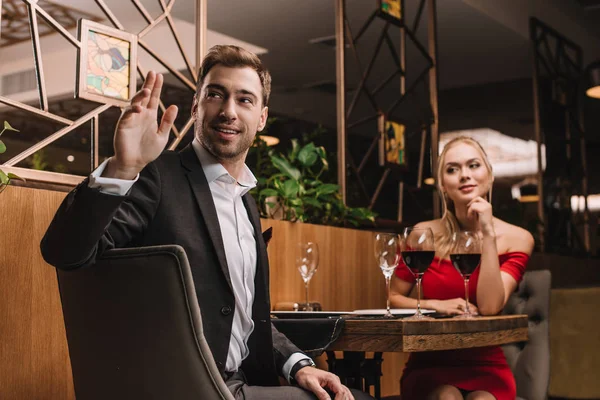 Handsome man calling waiter while sitting with girlfriend in restaurant — Stock Photo