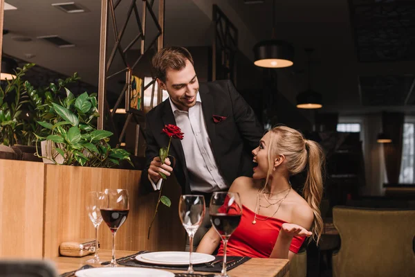 Guapo novio dando rojo rosa a sorprendido novia en restaurante - foto de stock