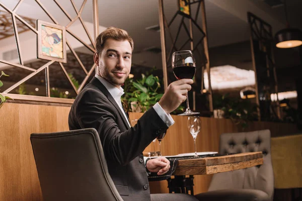 Hombre guapo sosteniendo vaso con vino tinto mientras está sentado en el restaurante - foto de stock