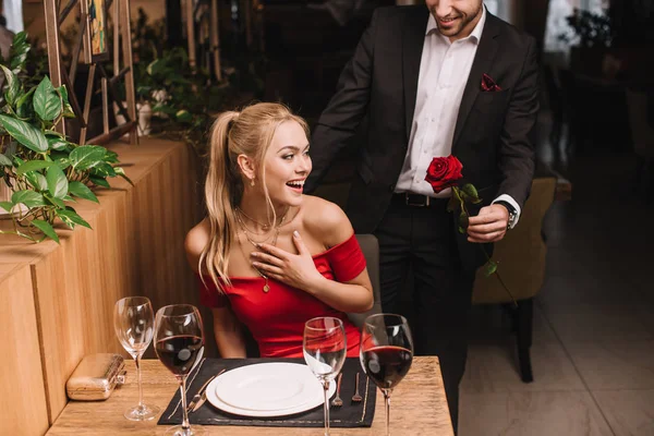 Novio dando rojo rosa a sorprendido novia en restaurante - foto de stock