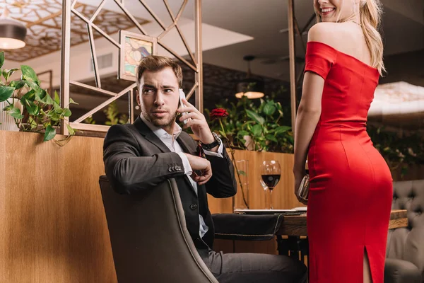 Hombre guapo hablando en el teléfono inteligente cerca de novia en vestido rojo — Stock Photo