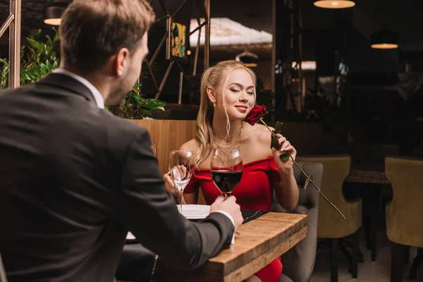 Attractive woman smelling rose while sitting in restaurant with boyfriend — Stock Photo