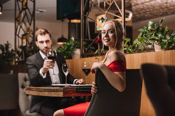 Foco seletivo de mulher atraente sentado no restaurante com namorado bonito em segundo plano — Fotografia de Stock