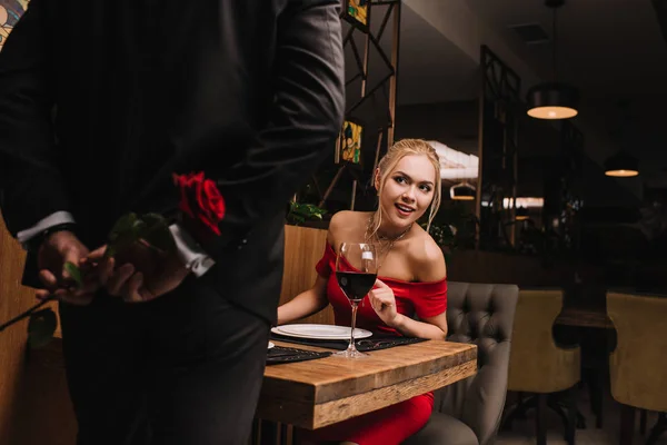 Curious girl looking at man hiding red rose in restaurant — Stock Photo