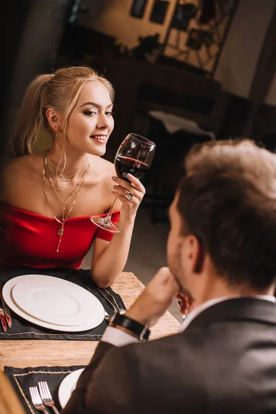 Foco seletivo de mulher atraente segurando vidro com vinho e flertando enquanto olha para o homem no restaurante — Fotografia de Stock