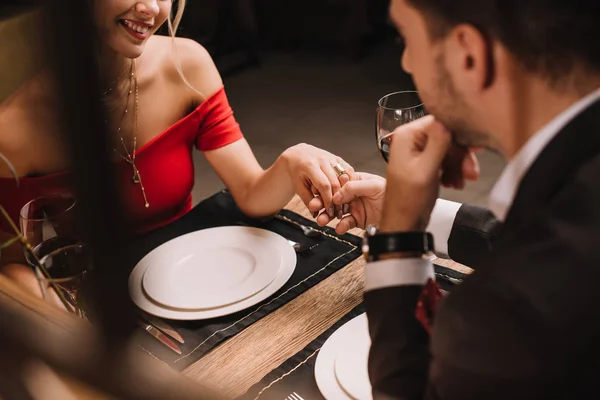 Vista recortada de la pareja cogida de la mano en el restaurante durante la cena - foto de stock