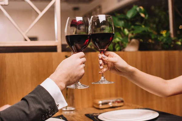 Vista recortada de una pareja de tostadas con copas de vino tinto en el día de San Valentín - foto de stock