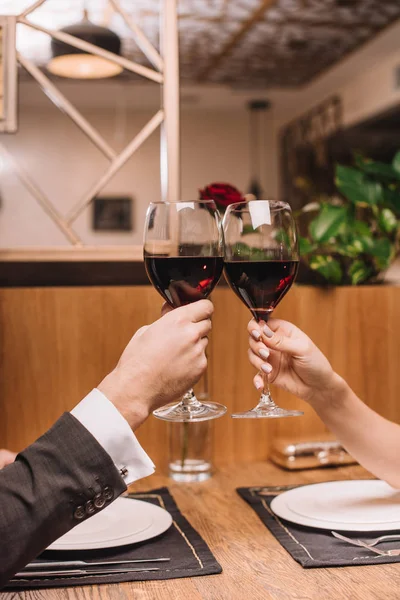Vista recortada de pareja tintineo con copas de vino tinto durante la cita romántica - foto de stock