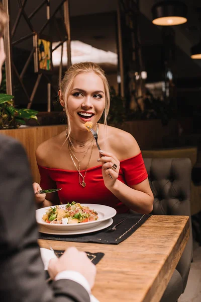 Mulher sorrindo comer salada enquanto se senta com namorado no restaurante — Fotografia de Stock