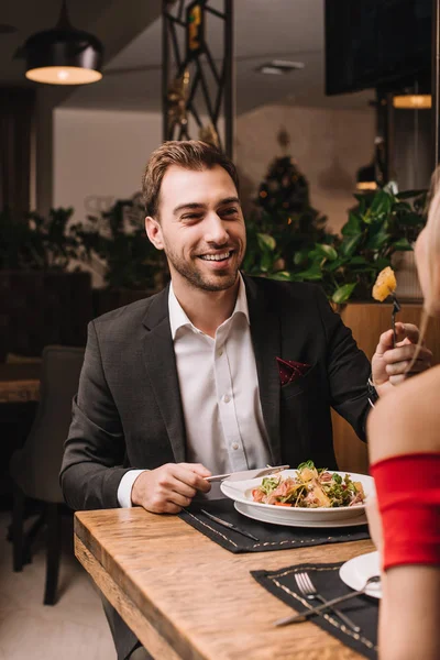 Handsome man feeding girlfriend with salad in restaurant — Stock Photo