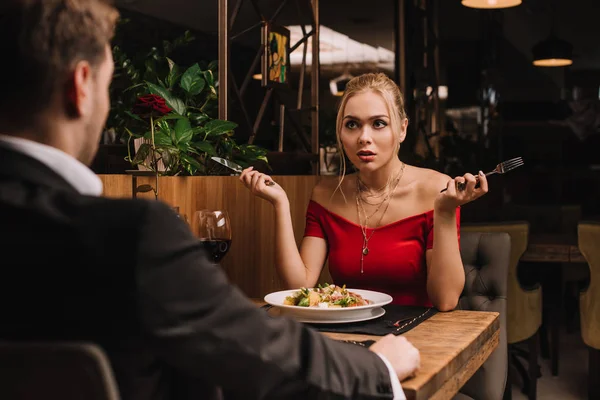 Mujer infeliz mirando al novio mientras sostiene cubiertos en el restaurante - foto de stock