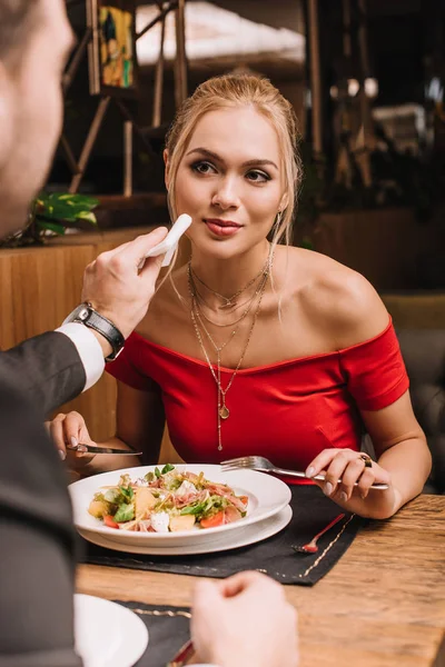 Namorado esfregando boca de mulher loira atraente com guardanapo no restaurante — Fotografia de Stock