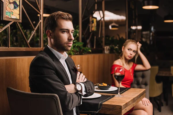 Selective focus of man sitting with crossed arms near girlfriend after quarrel in restaurant — Stock Photo