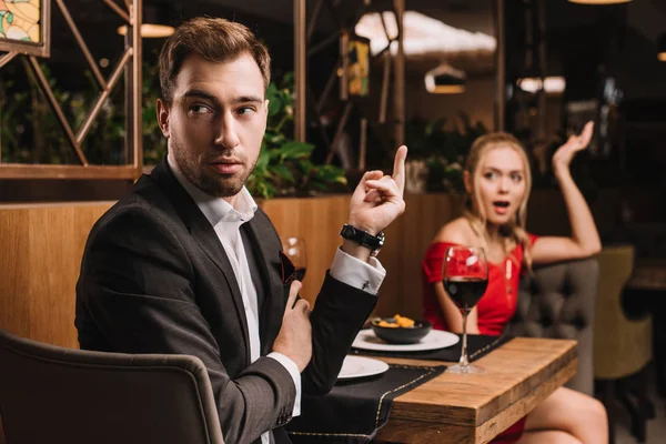 Selective focus of offended man showing middle finger to shocked girlfriend in restaurant during dinner — Stock Photo