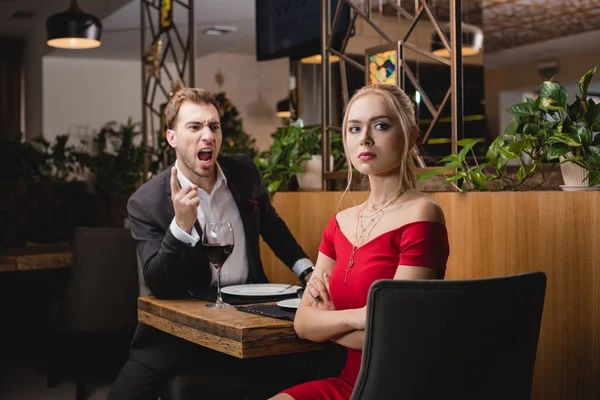 Selective focus of offended woman sitting with crossed arms near screaming boyfriend in restaurant — Stock Photo