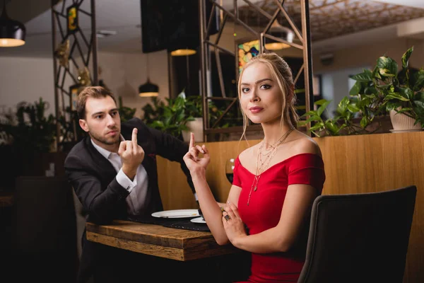 Emotional couple showing middle fingers to each other in restaurant during dinner — Stock Photo