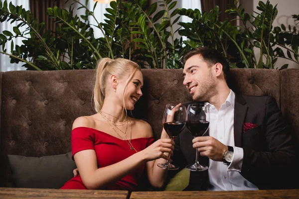 Atractiva mujer riendo mientras brindar con copa de vino tinto con novio en restaurante - foto de stock