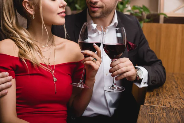 Cropped view of man and woman holding glasses with red wine — Stock Photo