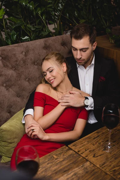 Handsome man hugging attractive woman while sitting in restaurant — Stock Photo