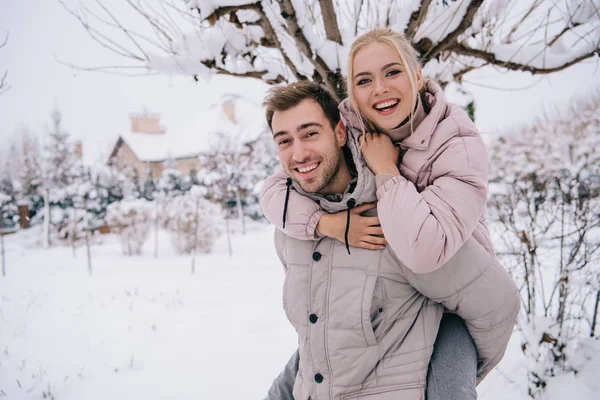 Sonriente hombre llevando atractiva mujer rubia en la espalda en invierno - foto de stock