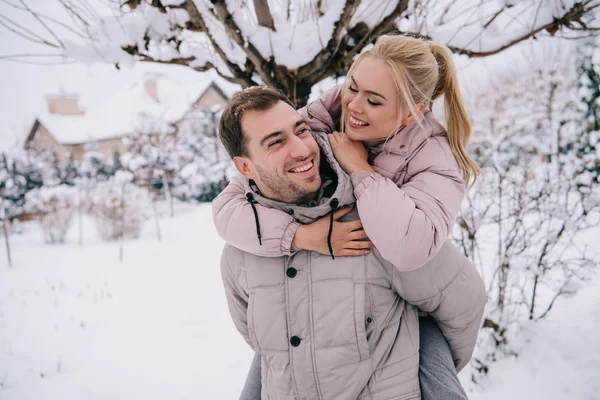 Namorado alegre carregando atraente menina loira de volta no inverno — Fotografia de Stock