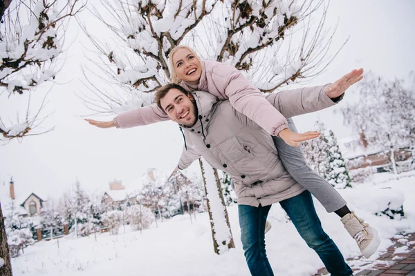 Fidanzato giocoso portando ragazza attraente sul retro in inverno — Foto stock