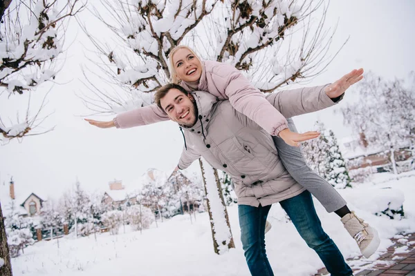 Novio juguetón llevando chica atractiva en la espalda en invierno - foto de stock