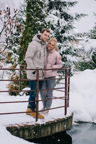 Feliz pareja mirando a la cámara y abrazándose en el frío parque de invierno - foto de stock