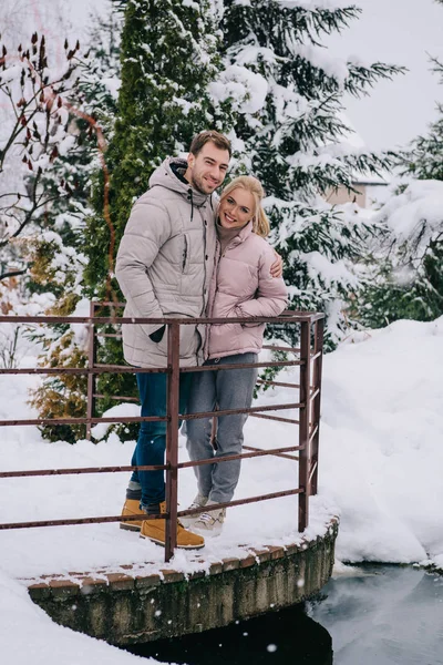 Coppia felice guardando la fotocamera e abbracciarsi nel freddo parco invernale — Foto stock