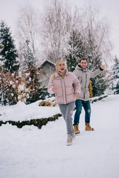 Donna gioiosa in esecuzione da fidanzato giocoso lancio palla di neve in inverno — Foto stock