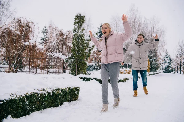 Mulher alegre correndo de namorado jogando bola de neve no inverno — Fotografia de Stock