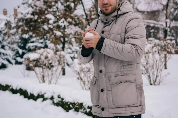 Vista ritagliata dell'uomo che tiene la palla di neve nelle mani in inverno — Foto stock