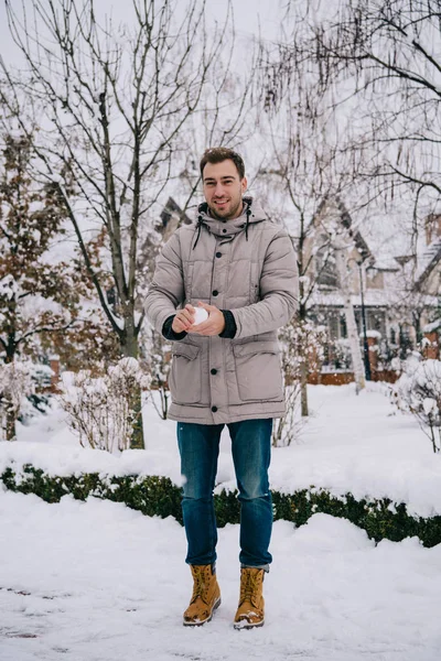 Homme joyeux tenant boule de neige dans les mains en hiver — Photo de stock