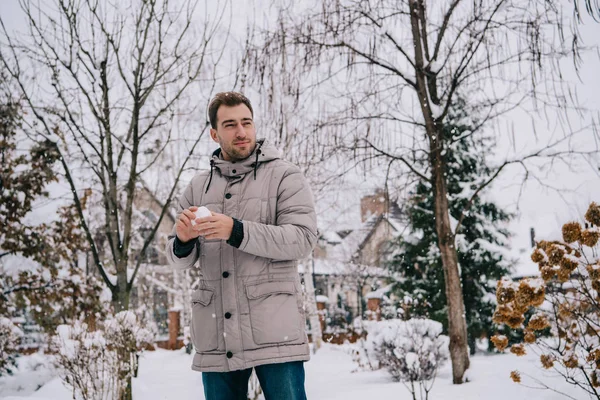 Homem bonito segurando bola de neve nas mãos no inverno — Fotografia de Stock