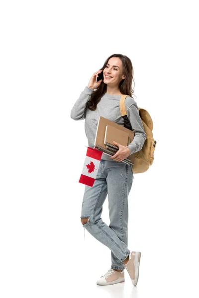 Female student with notebooks talking on smartphone and holding canadian flag isolated on white — Stock Photo