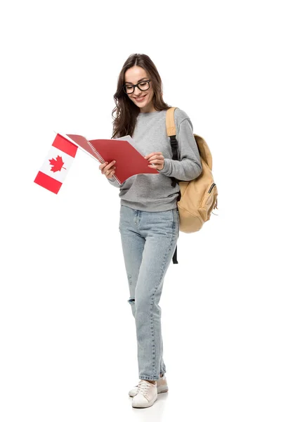 Estudante do sexo feminino em óculos segurando bandeira canadense e olhando para notebook isolado em branco — Fotografia de Stock