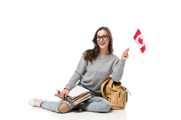 Счастливая студентка, сидящая с канадским флагом и блокнотами, изолированными на белом — стоковое фото