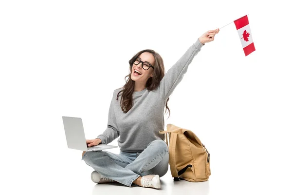 Estudiante sentada con laptop y animando con bandera canadiense aislada en blanco - foto de stock