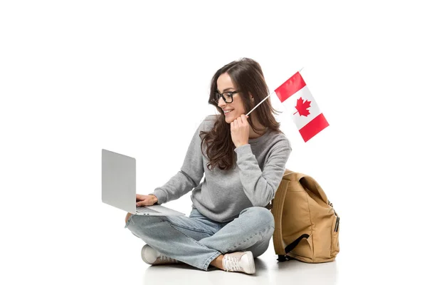 Estudante do sexo feminino sentado com bandeira canadense e usando laptop isolado no branco — Fotografia de Stock