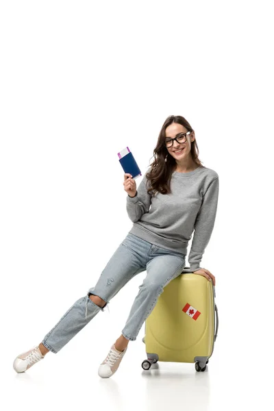 Mujer feliz sentada en la maleta con pasaporte y billetes de avión aislados en blanco, concepto de viaje - foto de stock
