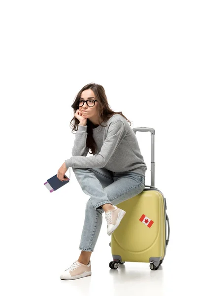 Pensive woman sitting on suitcase with passport and air tickets isolated on white, travel concept — Stock Photo