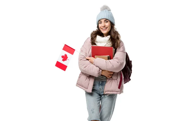 Heureuse étudiante en vêtements d'hiver avec drapeau canadien et cahiers isolés sur blanc, étudiant à l'étranger concept — Photo de stock