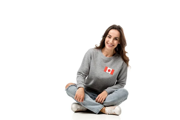 Glückliche Frau mit Abzeichen der kanadischen Flagge sitzt und in die Kamera schaut, isoliert auf weiß — Stockfoto
