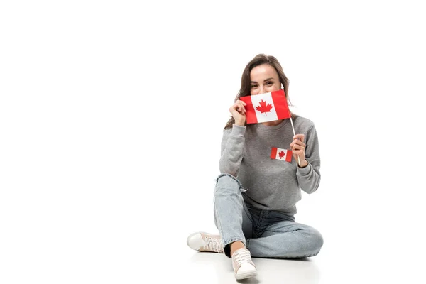 Woman with maple leaf badge sitting and holding canadian flag isolated on white — Stock Photo