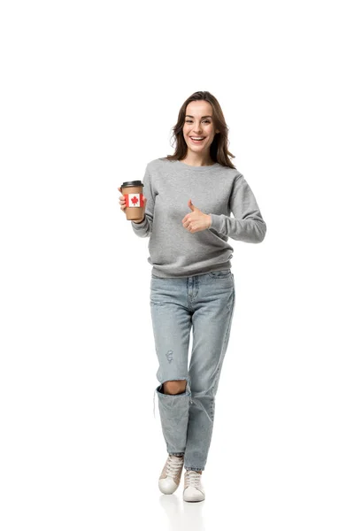 Mujer mostrando el pulgar hacia arriba y sosteniendo la taza de café con pegatina de bandera canadiense aislado en blanco - foto de stock