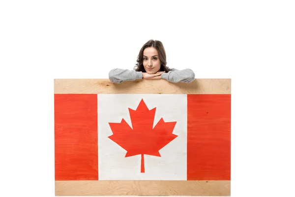 Donna seduta dietro tavola di legno con bandiera canadese e guardando la fotocamera isolata sul bianco — Foto stock