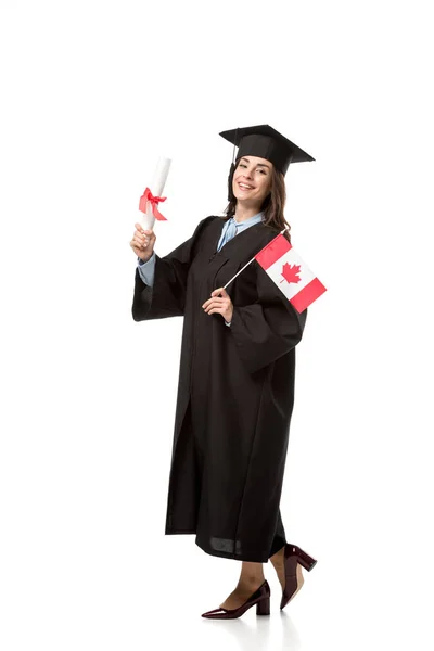 Feliz estudiante en vestido académico sosteniendo bandera canadiense y diploma aislado en blanco - foto de stock